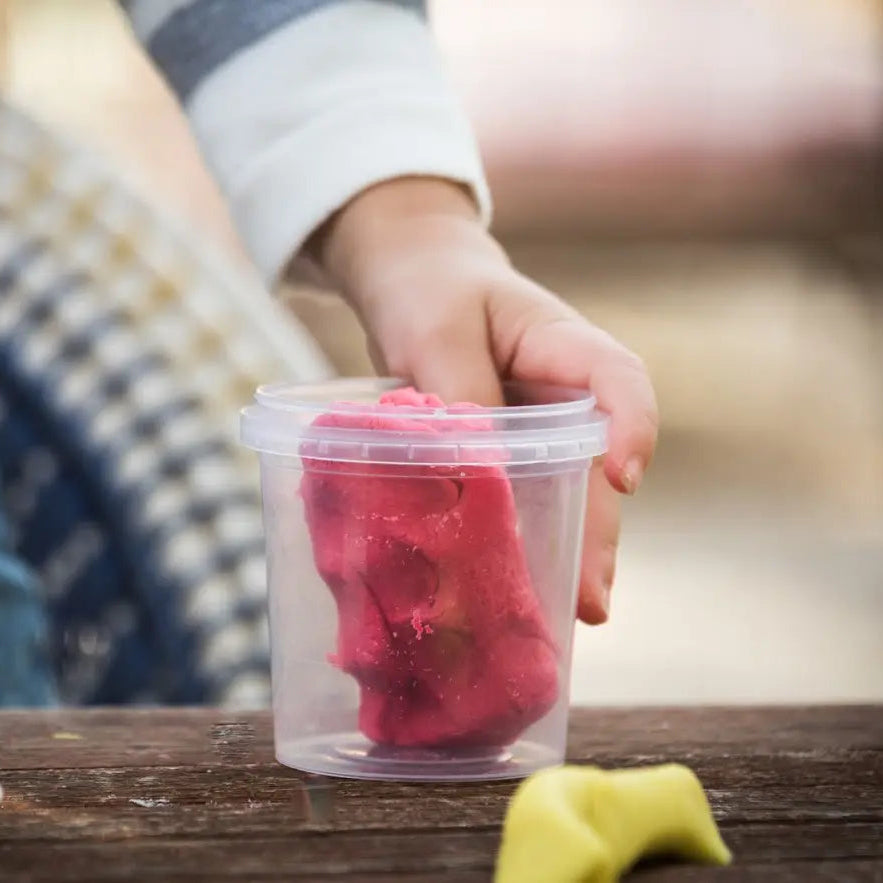 Main d'enfant plongeant dans un pot de pâte à modeler rouge